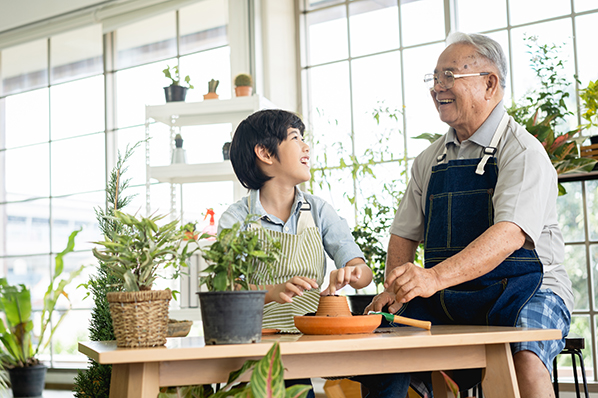 Older man laughing with young grandson while standing re-potting house plants.